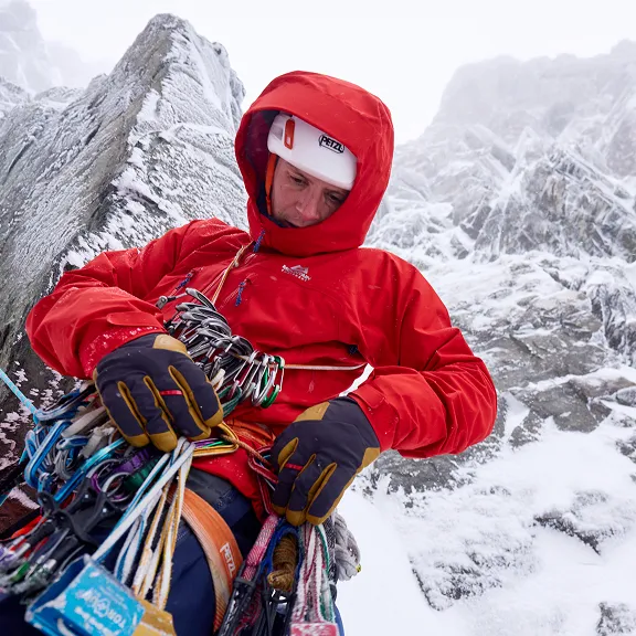 Ein Kletterer mit viel Equipment sitzt auf einem Felsvorsprung in verschneiter Bergkulisse.
